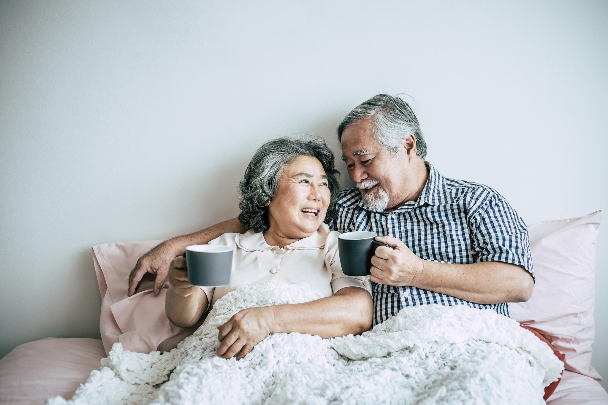 Couple smiling and drinking tea in bed