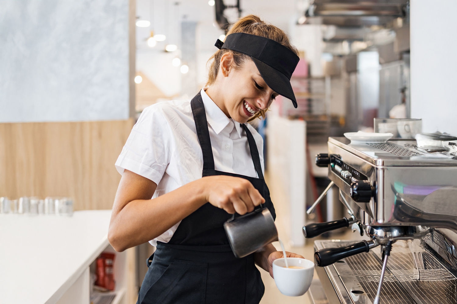 Beautiful and happy young female worker working in a bakery or fast food restaurant and using coffee machine. Positive people in small business concept.