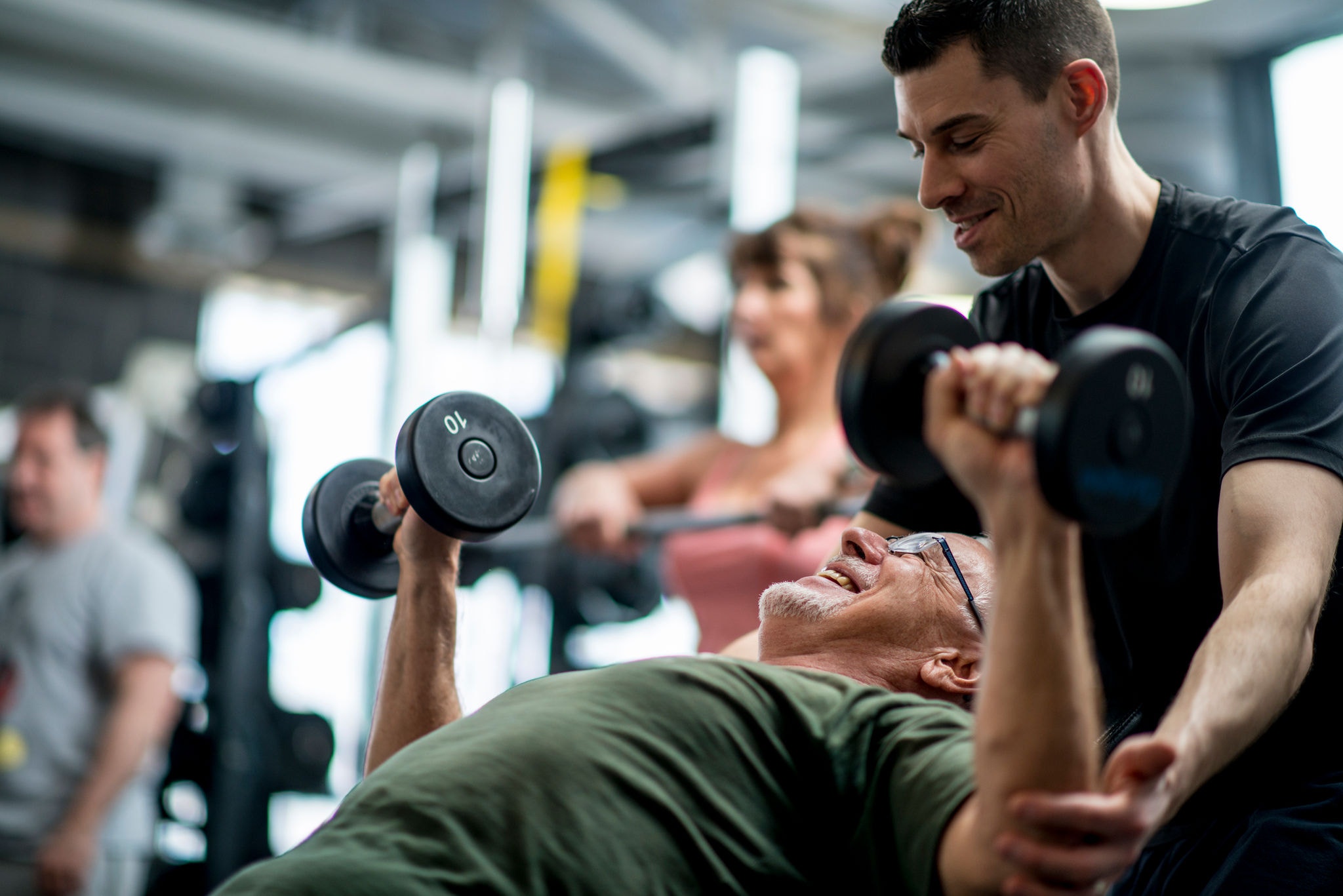 Senior man lifting weights with the guidance of the trainer