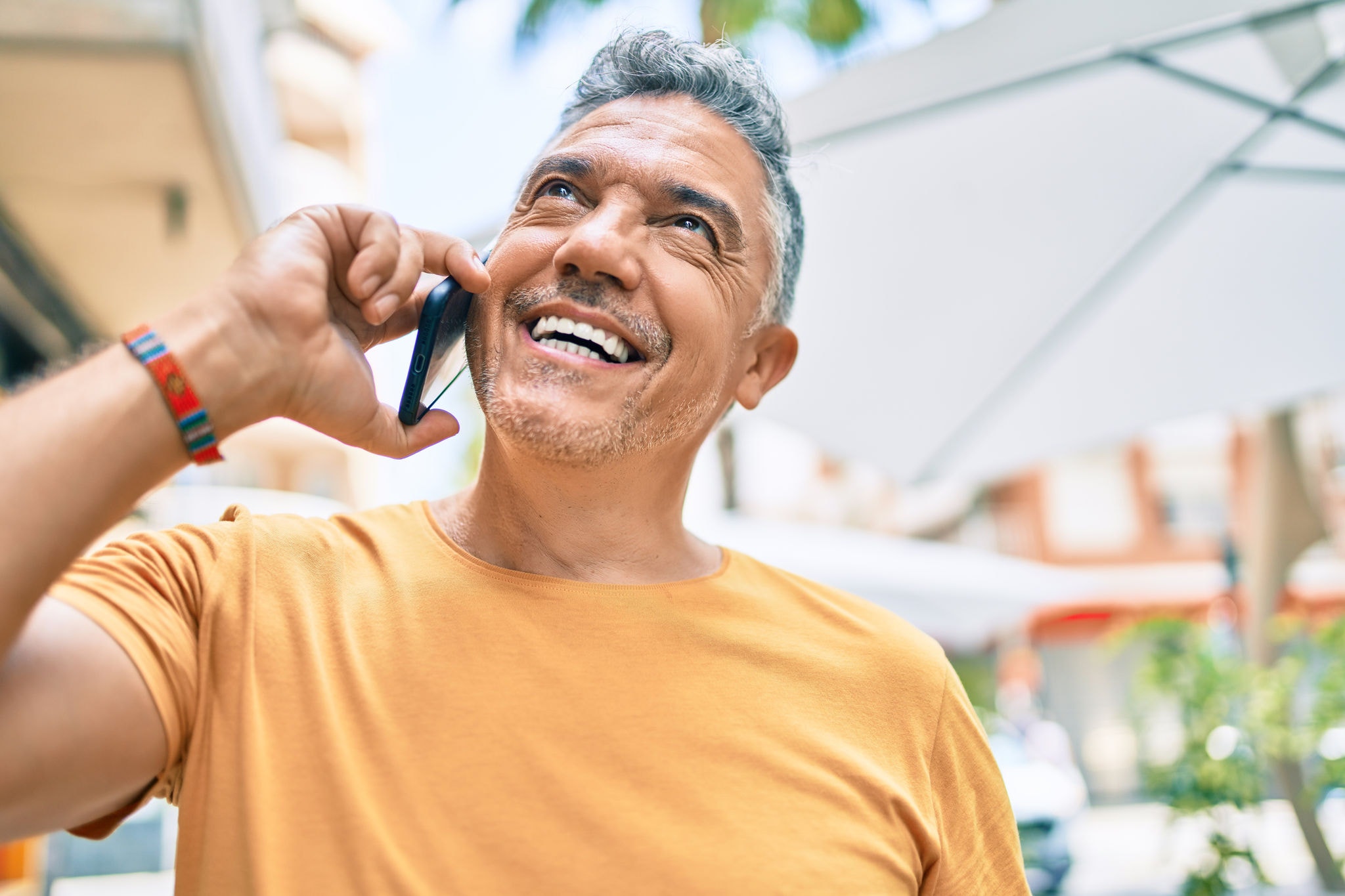 Middle age grey-haired man smiling happy talking on the smartphone at street of city.