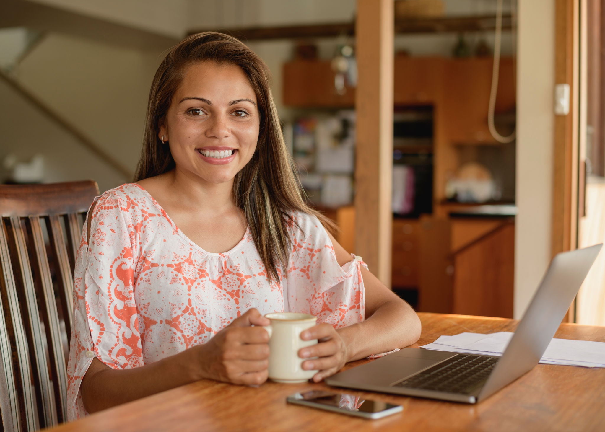 Woman in her 20s smiling towards camera with mug, working from home