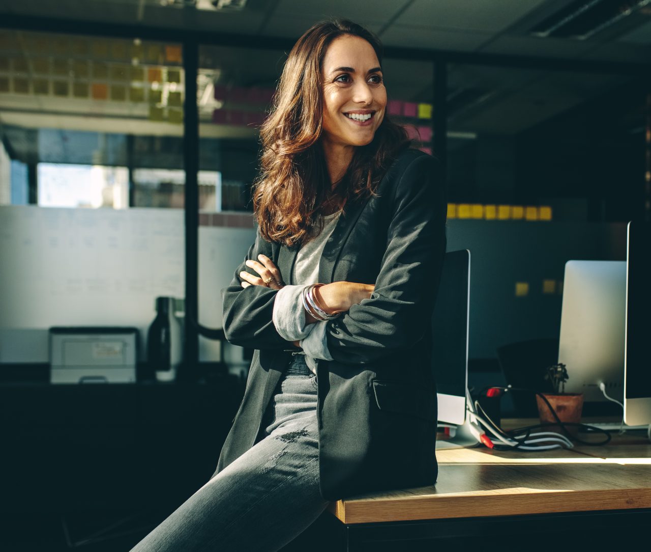 Smiling businesswoman sitting on her desk. Female business professionals sitting in her office looking away and smiling.