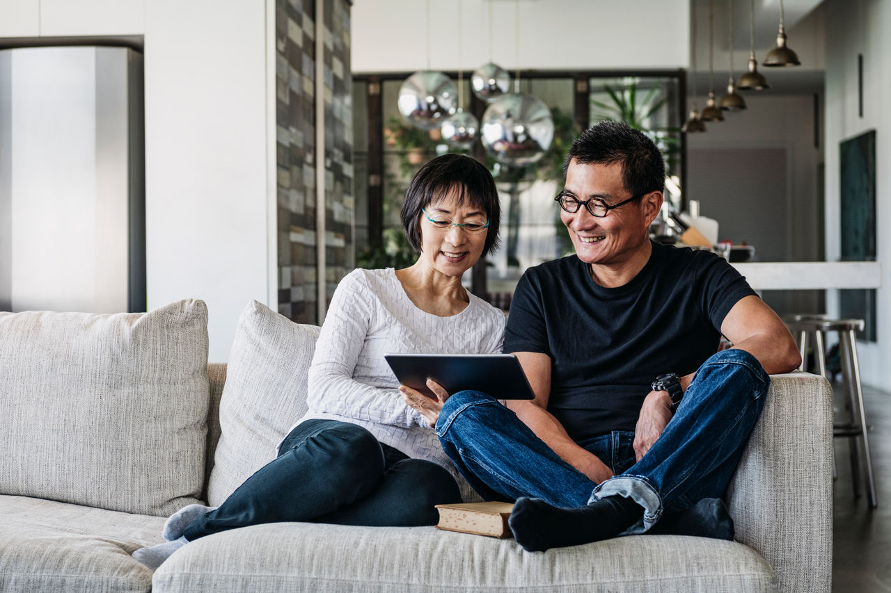 Senior woman and mature man using digital tablet at home in living room, talking online, facetime, social media
