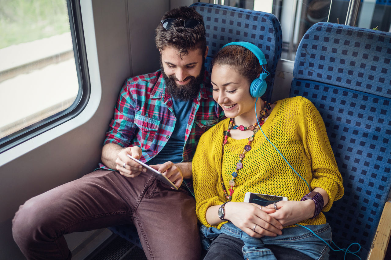 Attractive happy couple listening to music and browsing on the tablet while travelling