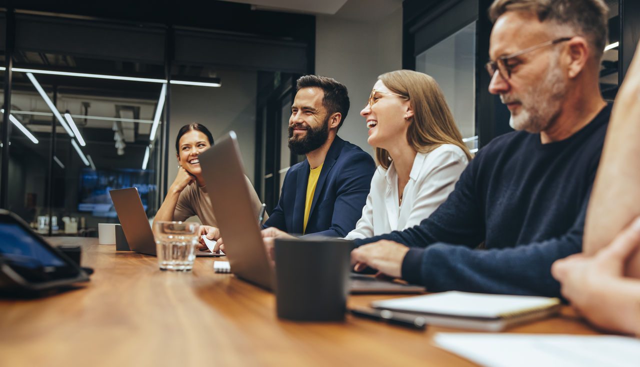 Positive businesspeople having a meeting in a boardroom. Group of happy businesspeople smiling while working together in a modern workplace. Diverse business colleagues collaborating on a project.