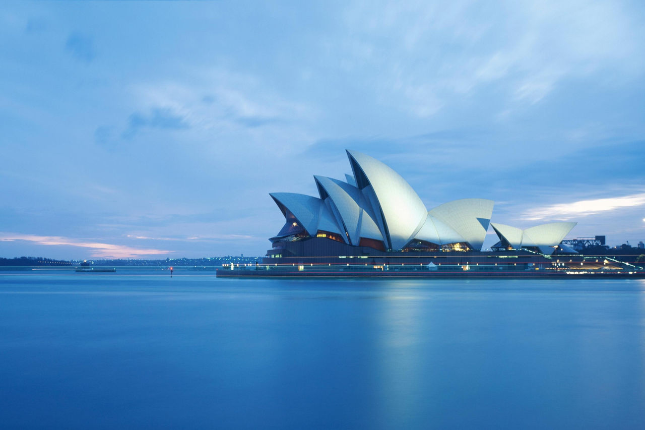Sydney Opera House against calm harbour water and cloudy sky at sunrise