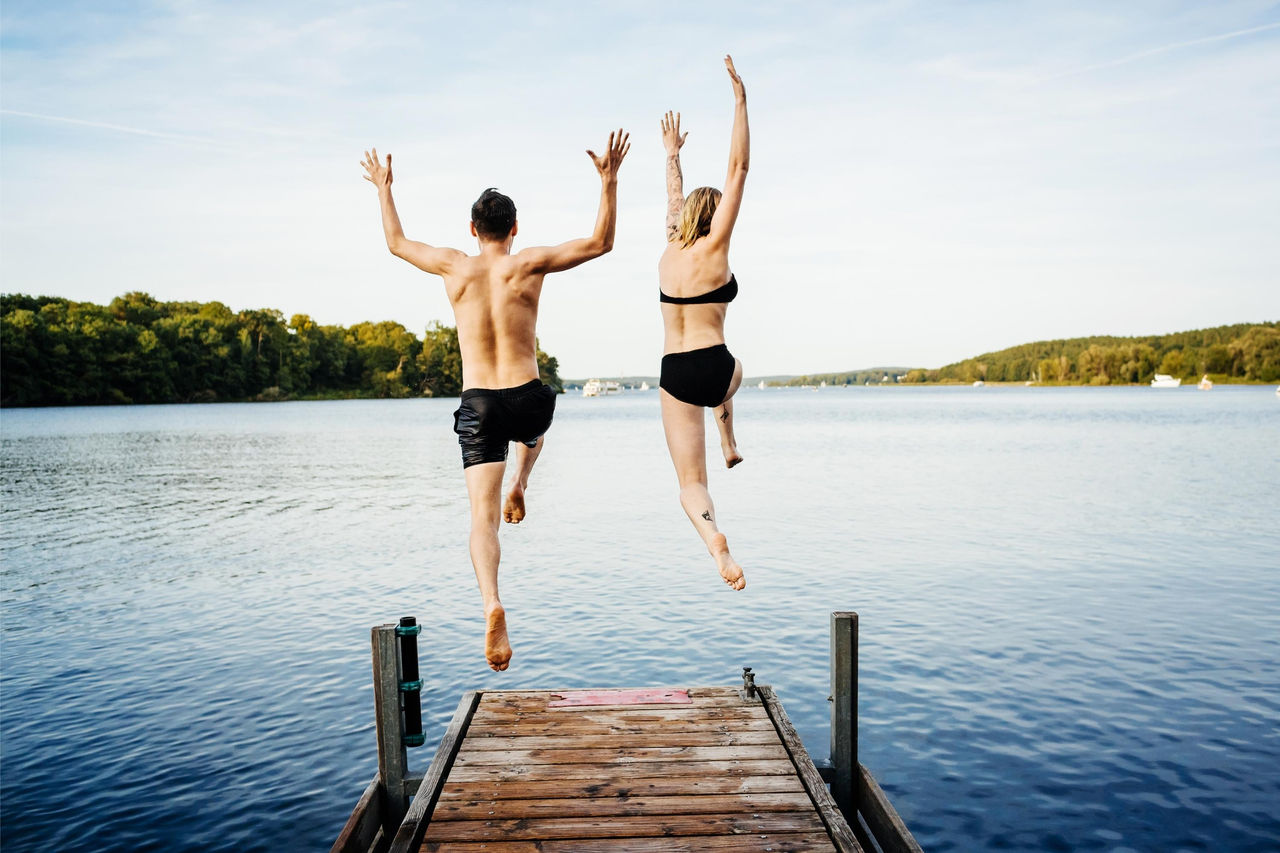 Man and woman jumping off a jetty into the water