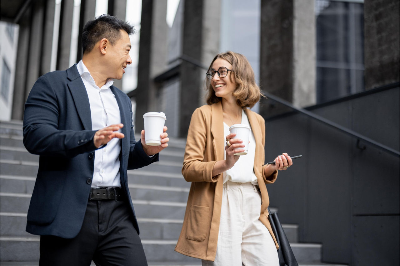 Man and woman colleagues walking down stairs in an office building holding coffee