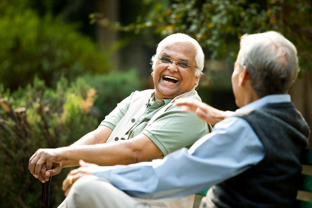 Two retired elderly men sitting on a park bench and having fun