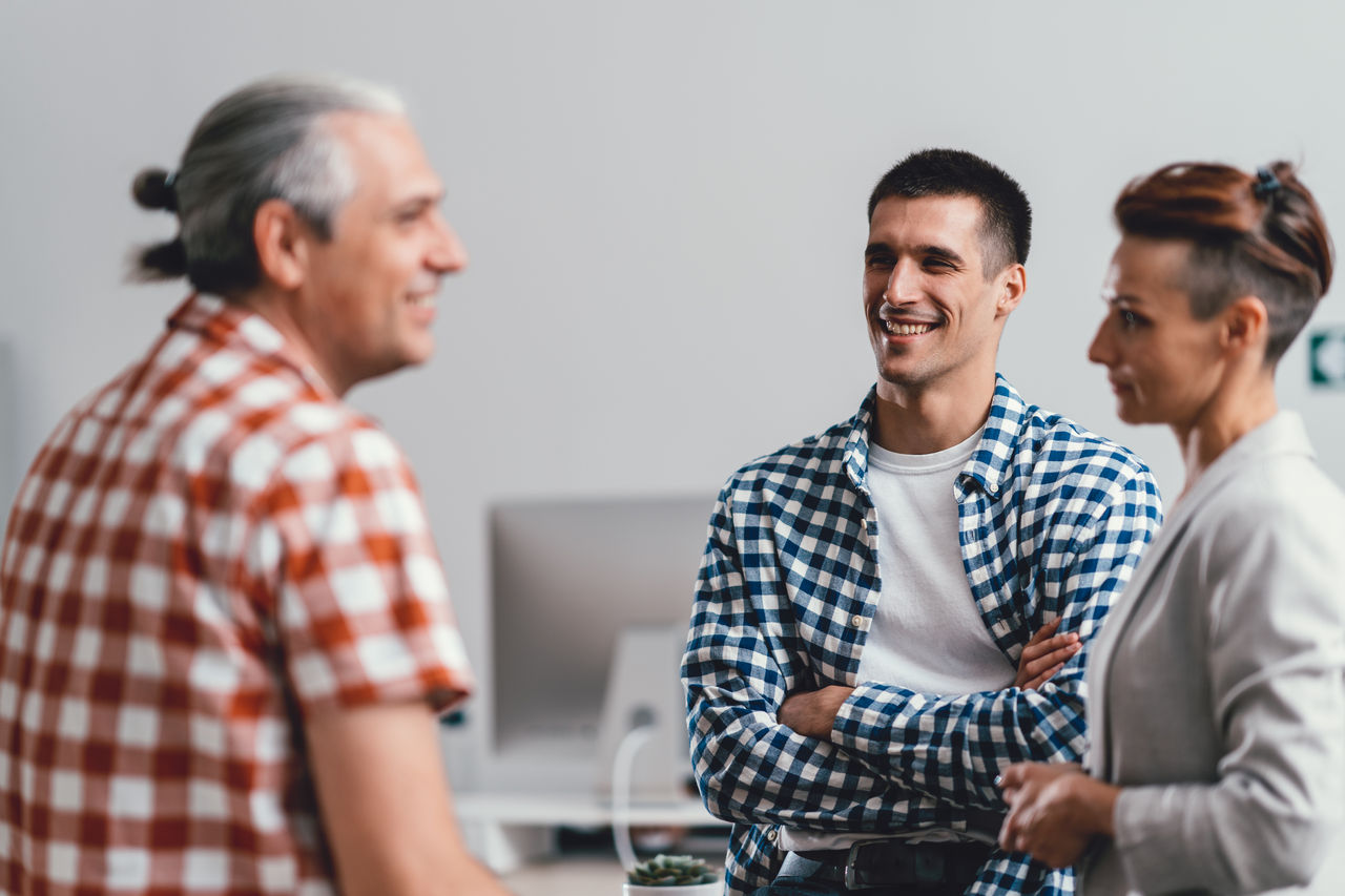 Young businessman wearing plaid shirt and smiling with colleagues at the office