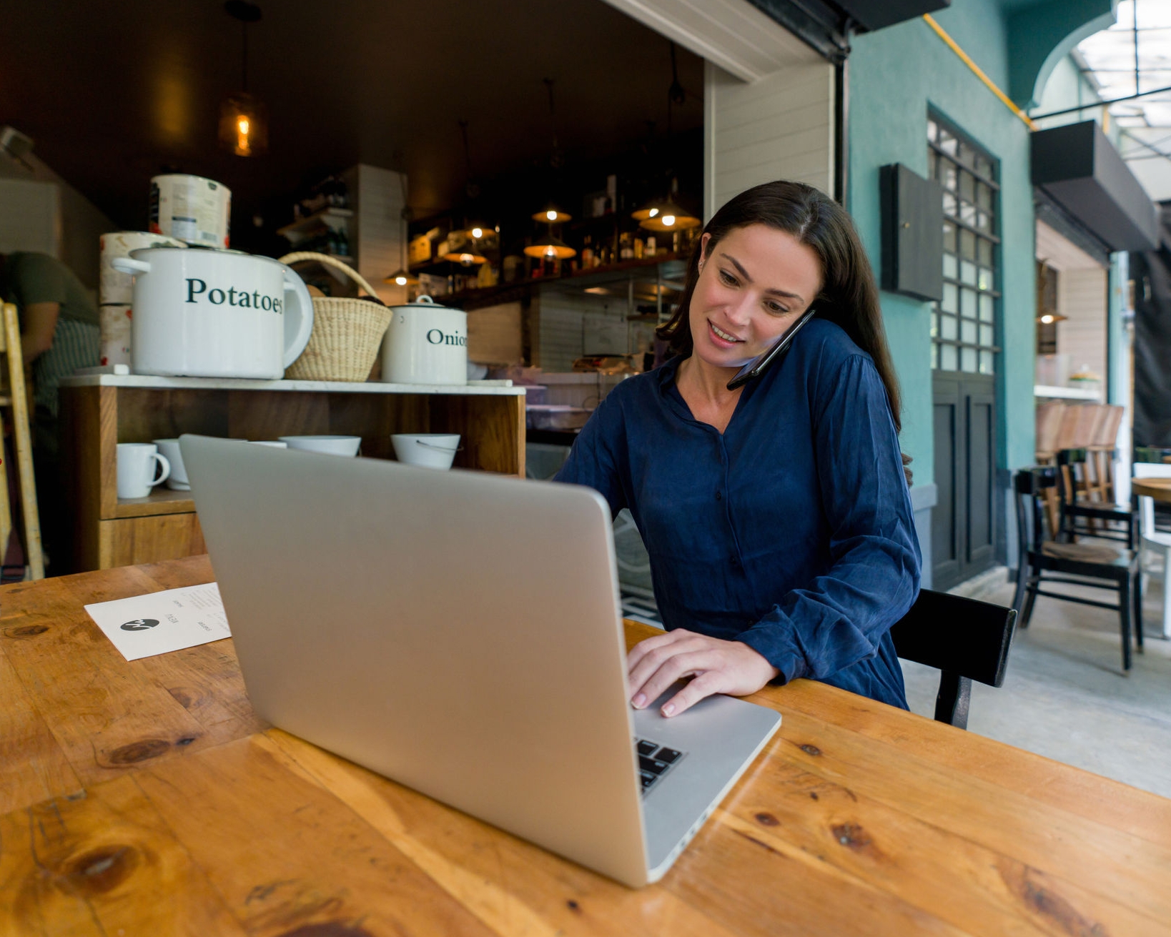 Latin American female entrepreneur working at a coffee shop on her laptop while talking on the phone